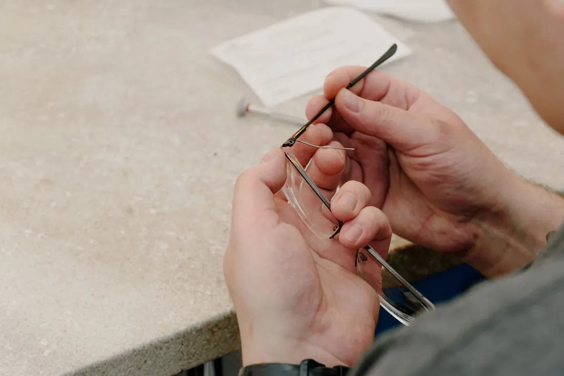 Manos montando una varilla sobre el frente de unas gafas en el banco de un taller